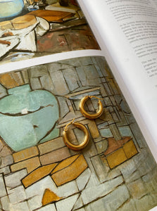 18 karat gold plated hoop earrings laying on a book