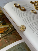 Load image into Gallery viewer, 18 karat gold plated silver round necklace with a bird in the middle laying on a book
