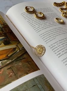 18 karat gold plated silver round necklace with a bird in the middle laying on a book